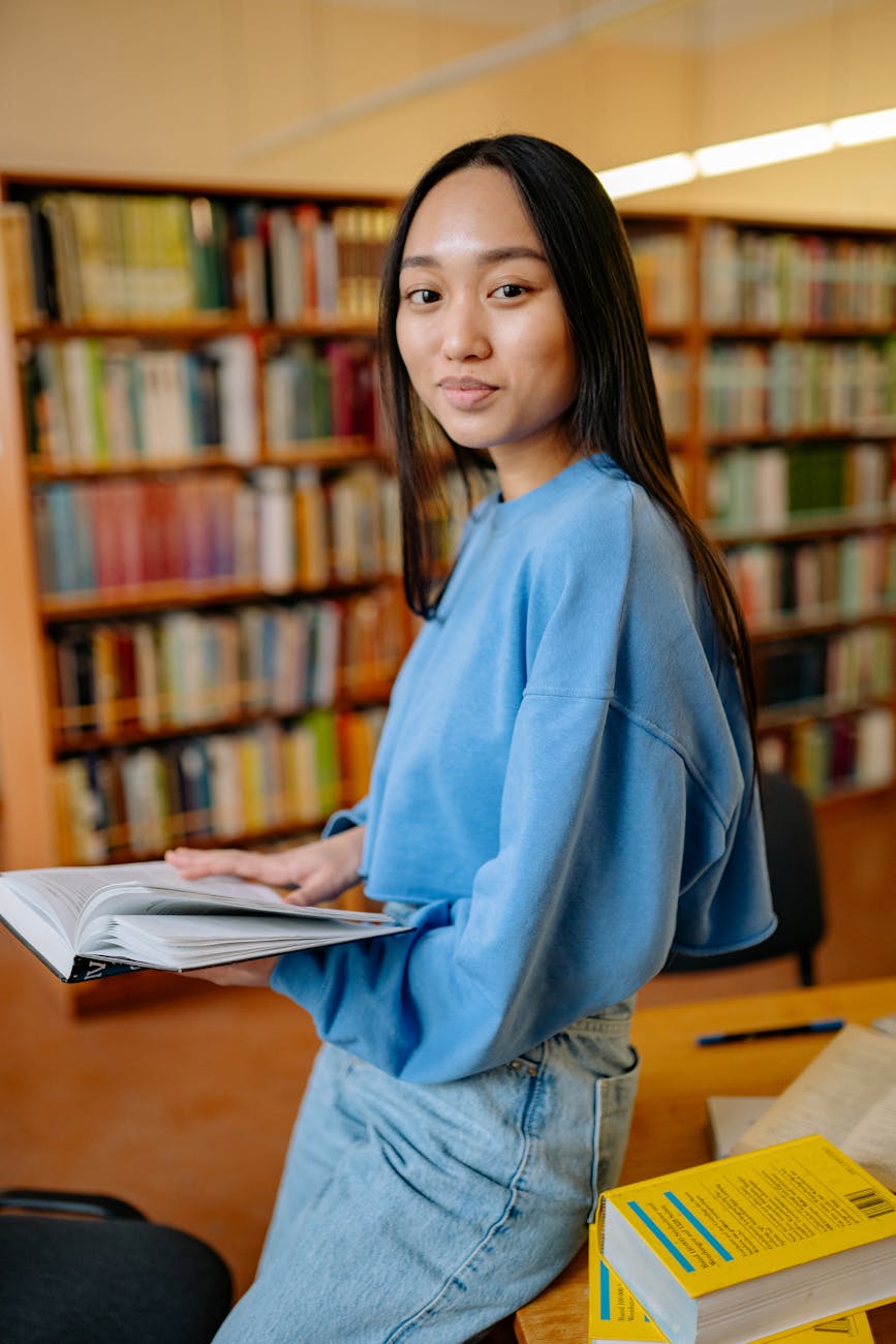 woman in blue long sleeve shirt holding a book smiling